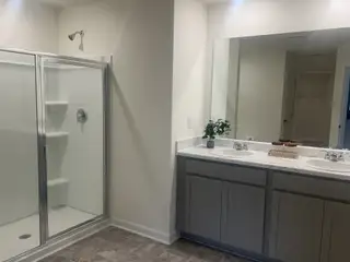 Model Home A modern bathroom featuring a sleek glass-enclosed shower, dual sinks, and ample cabinetry for storage.