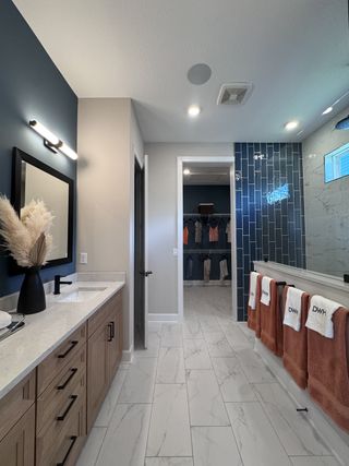 A modern bathroom featuring dual sinks, blue accent tiles, and sleek cabinetry leading to a spacious walk-in closet.