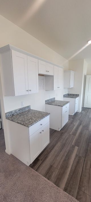Model Home A modern kitchen with white cabinets, granite countertops, and dark wood flooring.