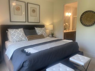 A cozy bedroom with a plush bed, decorative pillows, modern wall art, and an ensuite bath featuring elegant lighting and dark wood vanity.