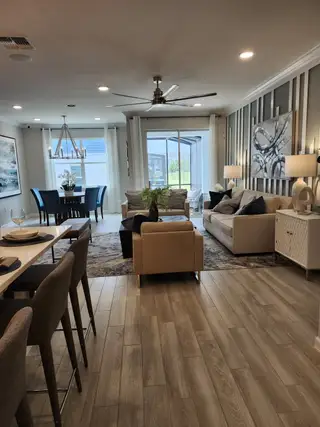 An elegant living area with wood flooring, modern decor, and stylish furnishings, leading to a bright dining space with large windows.