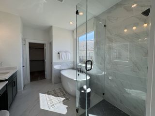 A bright bathroom featuring a freestanding tub, glass shower, and marble tiles with contemporary fixtures.