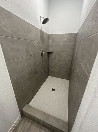 A sleek shower with large gray tiles, a modern showerhead, and a small storage ledge for convenience.