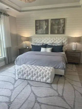 A cozy bedroom featuring a tufted bed, elegant artwork, soft lighting, and plush rugs for a serene ambiance.