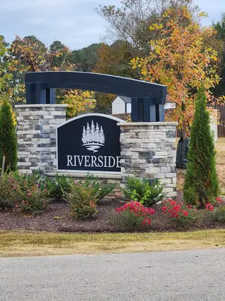 Charming stone entrance with lush landscaping in Riverside by RiverWILD Homes (Zebulon, NC).