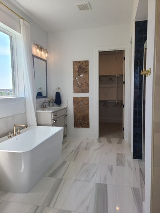 A luxurious bathroom featuring a freestanding tub, marble flooring, elegant fixtures, and chic wall decor.