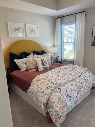 A vibrant kid’s bedroom with a mustard yellow headboard, colorful floral bedding, and playful equestrian artwork.