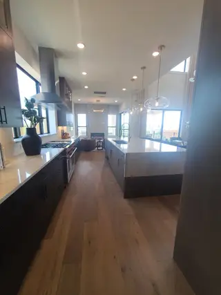 A sleek kitchen with dark cabinetry, pendant lighting, and a spacious island, featuring elegant wood flooring.