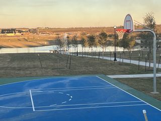 A vibrant outdoor basketball court overlooking a scenic pond and walking trails in Harvest Ridge by Brohn Homes (Elgin, TX).