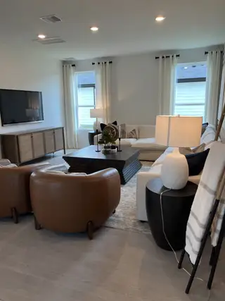 A cozy living room with a large sectional, leather chairs, a wooden coffee table, and soft lighting.