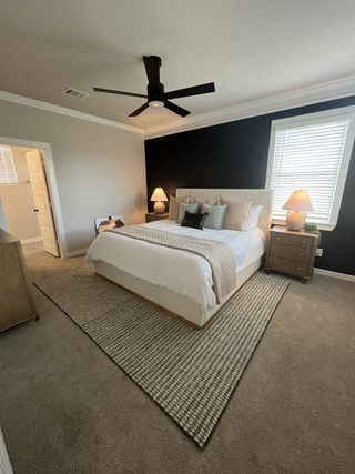 Model Home A cozy bedroom with a plush carpet, modern ceiling fan, and elegant bedside lighting.
