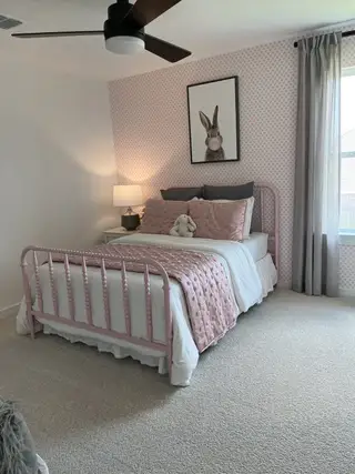 Cozy bedroom with a pink metal bed, patterned wallpaper, and plush bedding, accented by a whimsical bunny print.