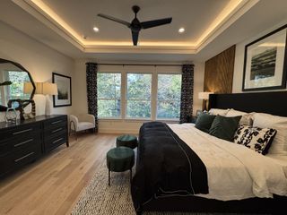Model Home A cozy bedroom featuring a large bed, layered lighting, elegant decor, and forest views through expansive windows.
