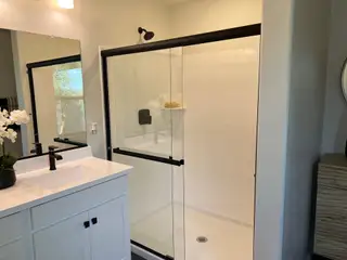 Model Home A modern bathroom with a sleek, glass-enclosed shower, white vanity, and elegant black fixtures.