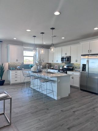 Model Home Modern kitchen with white cabinets, sleek stainless steel appliances, an island with seating, and stylish pendant lighting.