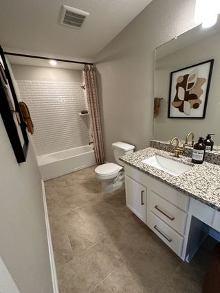A chic bathroom with granite countertops, tiled floors, and modern fixtures, complemented by elegant wall art.