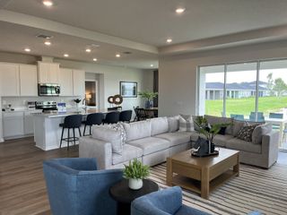 Model Home A spacious, open-concept living area with a cozy sectional, modern kitchen, and expansive windows overlooking a lush backyard.
