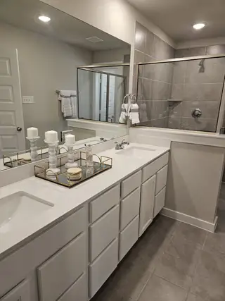 A sleek bathroom featuring a dual vanity, large mirror, and a modern glass-enclosed shower with stylish gray tile.