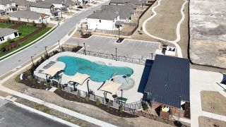 A stunning aerial view of the community pool at University Heights by Scott Felder Homes in Round Rock, TX, featuring shaded seating and a splash area.