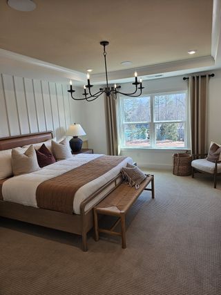 A cozy bedroom featuring a large bed, elegant chandelier, and soft, neutral decor with warm accents.