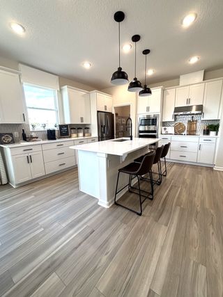 A modern kitchen with white cabinets, sleek countertops, pendant lighting, and wood-look flooring.