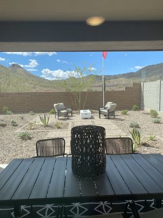 Model Home A stylish patio features wicker egg chairs, a wooden dining table with modern chairs, decorative lanterns, and a scenic mountain view beyond a brick wall.