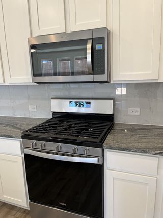 Features a modern gas stove and a built-in Whirlpool microwave. White cabinetry and marble-look backsplash create a sleek, bright aesthetic.