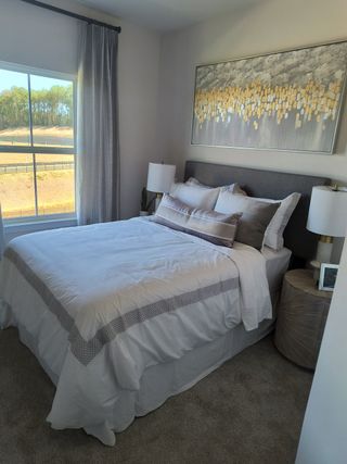 Model Home A cozy bedroom featuring a plush bed, elegant artwork, and soft lighting through a large window with serene views.