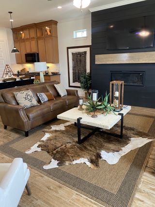 A cozy living room featuring a leather sofa, cowhide rug, rustic decor, and a modern fireplace against a shiplap accent wall.