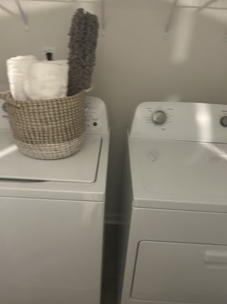 Model Home A functional laundry room with a modern washer, dryer, shelving, and a neatly arranged basket of towels.