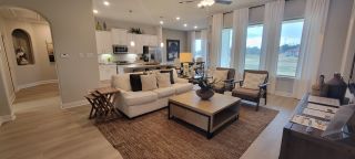 Model Home A cozy open-plan living area with neutral tones, plush seating, and large windows offering a serene outdoor view.