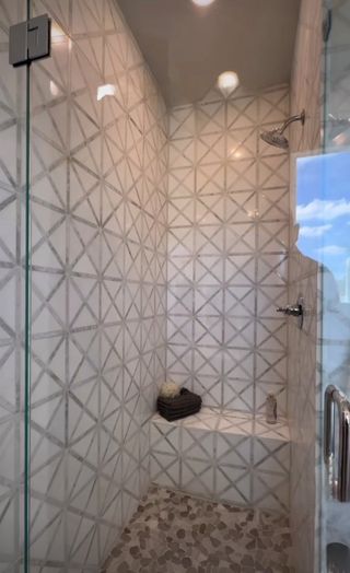 A modern shower with geometric wall tiles, pebble flooring, and a glass door for a sleek, contemporary look.