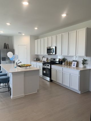 A modern kitchen with sleek white cabinets, stainless steel appliances, and a large island with blue bar stools.