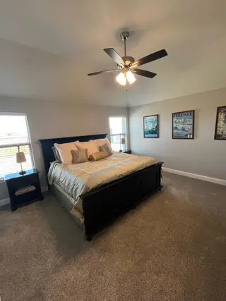 A cozy bedroom with a dark wood bed, plush carpeting, elegant decor, and a modern ceiling fan.
