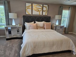 Model Home A cozy bedroom with a plush bed, mirrored nightstands, elegant lamps, and abstract artwork on a soft-toned wall.