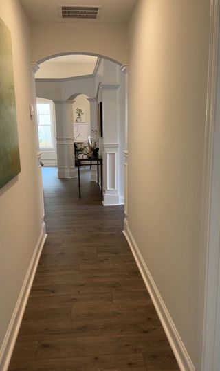 A long hallway with archways, wainscoting, and dark wood flooring in Covington by Castle Homes (Savoy Park, GA).