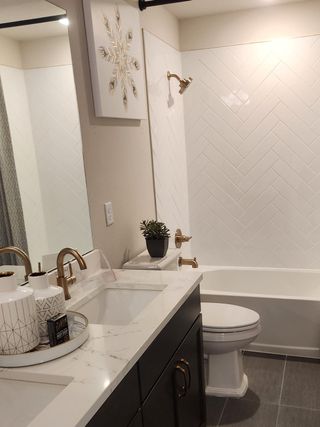 A contemporary bathroom with herringbone tile, marble countertop, gold fixtures, and elegant accents.