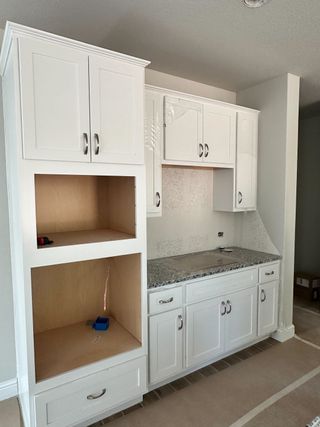 Model Home A sleek kitchen setup featuring white cabinetry with metallic handles and granite countertops, offering ample storage space.