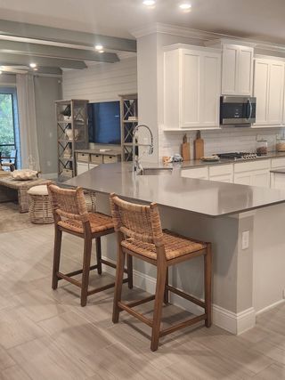 A modern kitchen featuring white cabinetry, sleek countertops, and woven bar stools, flowing into a cozy living area.