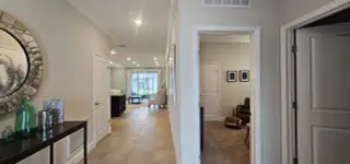 A welcoming hallway with tile flooring, decorative mirror, and natural light leading to a cozy living space.