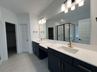 Model Home A sleek bathroom with dual sinks, black cabinetry, gold fixtures, and a glass-enclosed shower, offering a clean, modern design.
