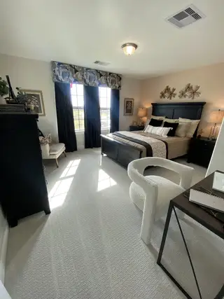 Model Home A cozy bedroom with a plush carpet, elegant black furniture, and expansive windows allowing ample natural light.