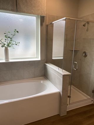 Model Home A bright bathroom featuring a spacious bathtub, glass-enclosed shower, and a window with elegant frosted glass.