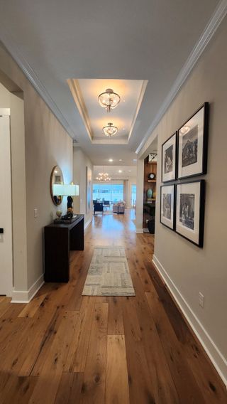 A welcoming hallway with recessed ceiling lighting, framed artwork, and warm hardwood floors leading to the main living area.