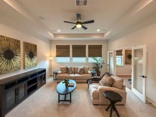 A cozy living room with plush seating, abstract wall art, and a ceiling fan, featuring natural light from large windows.