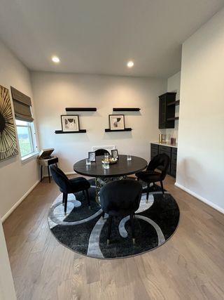 A modern dining area with a sleek round table, plush black chairs, and stylish wall shelves.