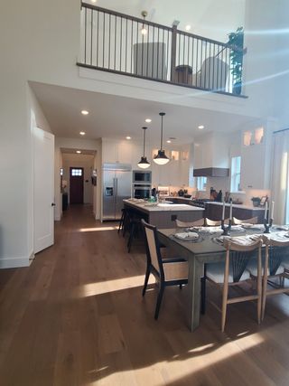 A modern open-plan kitchen with high ceilings, sleek island, and elegant dining area, featuring warm wood flooring.