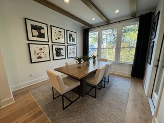 A modern dining area with a wooden table, beige chairs, abstract art, and large windows offering a serene view.