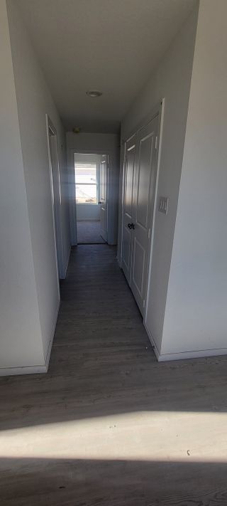 A bright hallway with light wood floors, white walls, and natural light streaming through a distant window.