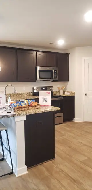 Model Home A modern kitchen with dark cabinets, granite countertops, stainless steel appliances, and warm wood flooring.